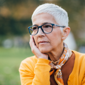 Older woman with glasses outside holding her face